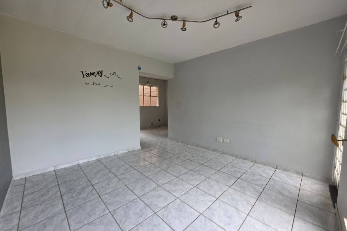 An empty living room featuring neutral tiled flooring, track lighting, and a security gate, offering a clean canvas for personalization.