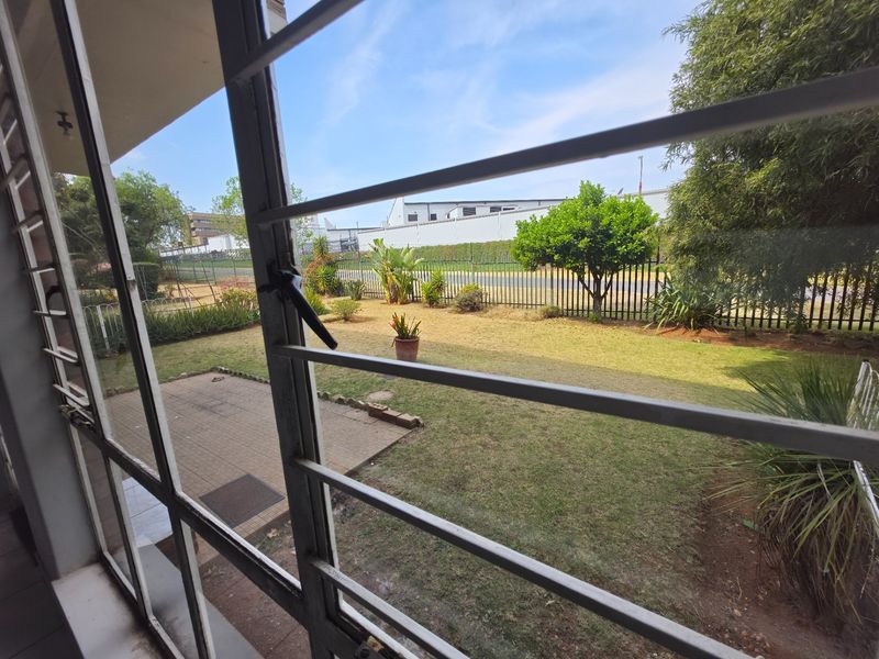 View from an interior window looking out onto a private garden area with a paved patio and perimeter fencing.
