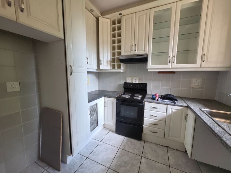 A functional kitchen featuring cream-colored cabinetry, granite countertops, a tiled backsplash, and a freestanding stove with an extractor fan.