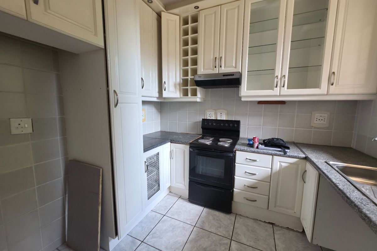 A functional kitchen featuring cream-colored cabinetry, granite countertops, a tiled backsplash, and a freestanding stove with an extractor fan.