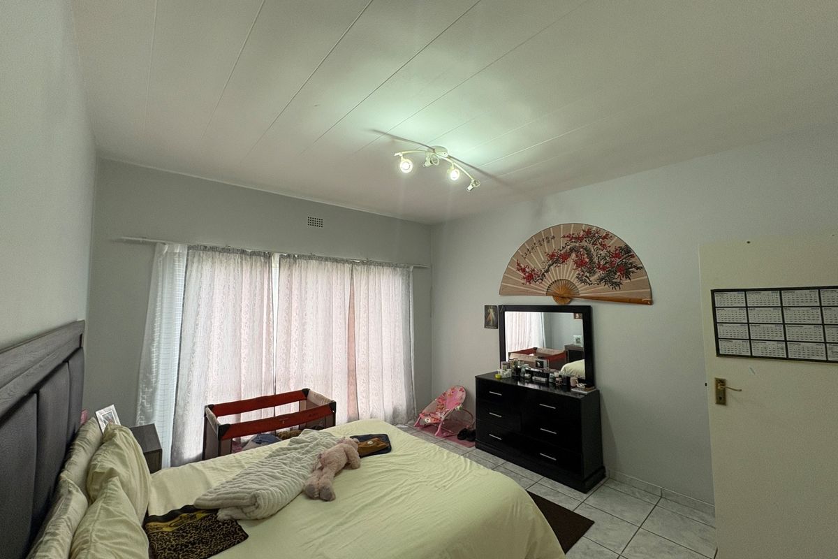 A spacious bedroom featuring tiled flooring, neutral wall finishes, and large windows with curtain rails, providing a functional and well-lit living space.