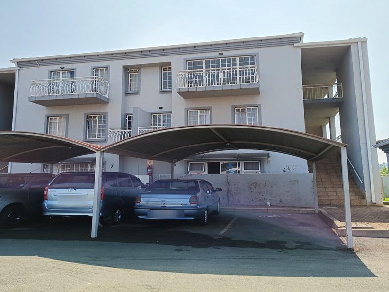 Exterior view of a multi-story apartment building featuring covered parking bays, balconies, and an external staircase.