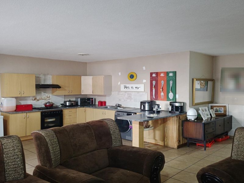 Open plan living area featuring a functional kitchen with laminate cabinetry, built-in oven, extractor fan, and a breakfast bar, finished with tiled flooring throughout.