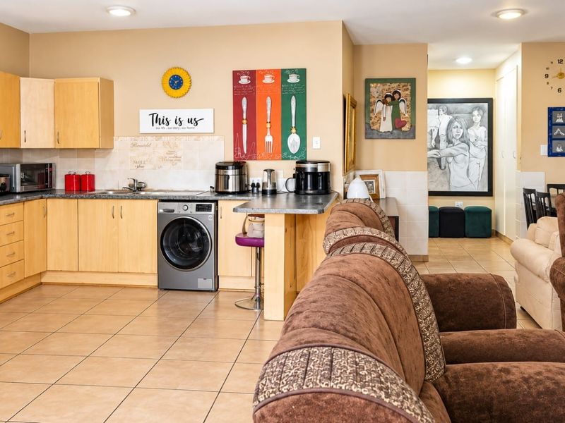 Open-plan living area featuring a functional kitchen with light wood cabinetry, tiled flooring, and integrated appliances, flowing into the adjacent living space.