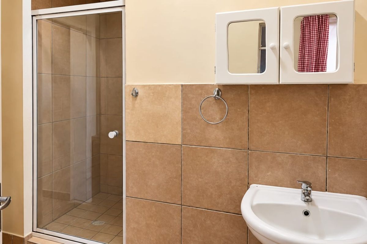 A functional bathroom featuring a tiled shower enclosure, a wall-mounted basin with a mixer tap, and a built-in medicine cabinet.