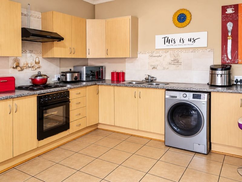 A functional kitchen featuring light wood laminate cabinetry, granite countertops, tiled flooring, and integrated appliances including an oven and extractor fan.