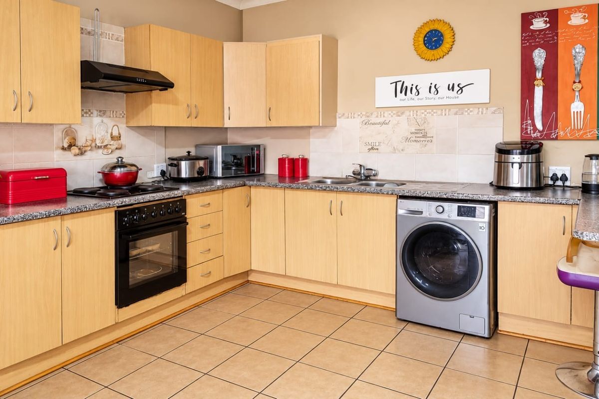 A functional kitchen featuring light wood laminate cabinetry, granite countertops, tiled flooring, and integrated appliances including an oven and extractor fan.