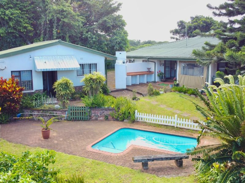 Rear view of the property featuring a swimming pool, brick paved patio area, built-in outdoor counter, and established garden surroundings.