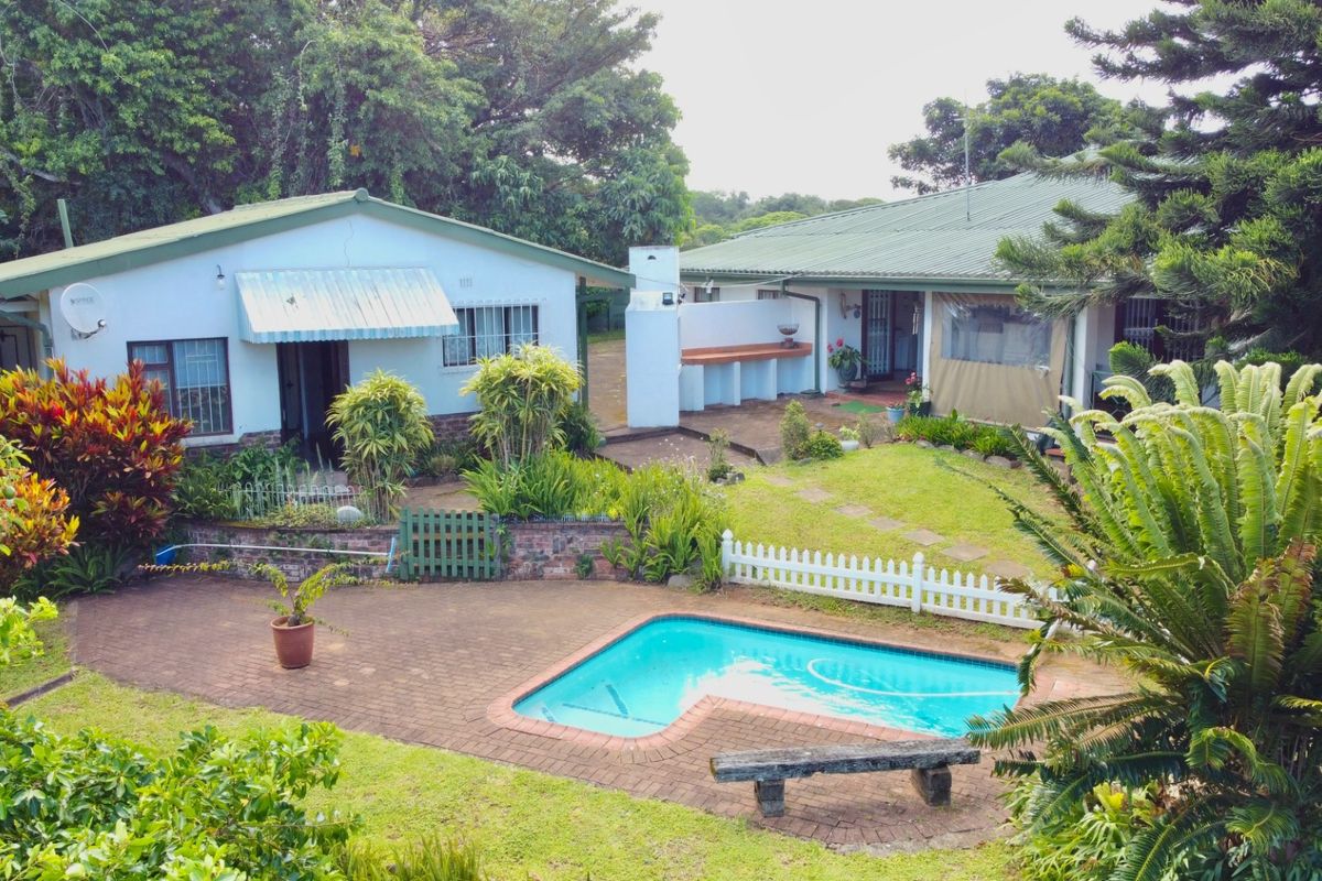Rear view of the property featuring a swimming pool, brick paved patio area, built-in outdoor counter, and established garden surroundings.
