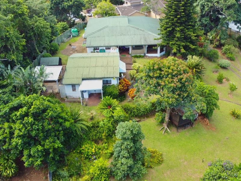 Aerial view of a residential property featuring a metal roof, established garden, and outdoor patio area set within a lush, green environment.