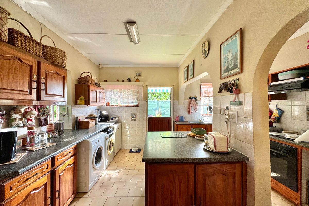A functional kitchen featuring wooden cabinetry, laminate countertops, tiled backsplash, and an integrated oven, with an adjacent archway leading to additional prep space.