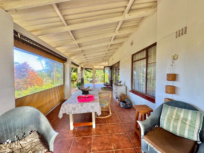 A covered patio area featuring tiled flooring, exposed beam ceiling, and outdoor roller blinds, offering a functional space for outdoor living.