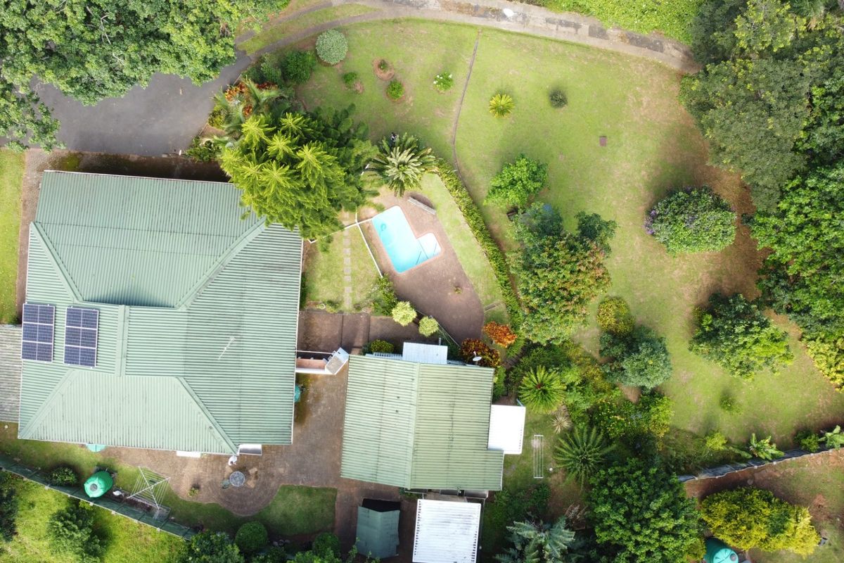 Aerial view of the property featuring a large garden, swimming pool, paved patio, and solar panels installed on the metal roof.