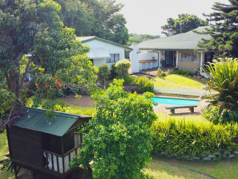 Rear view of the property featuring a swimming pool, landscaped garden, paved patio area, and a built-in outdoor braai facility.