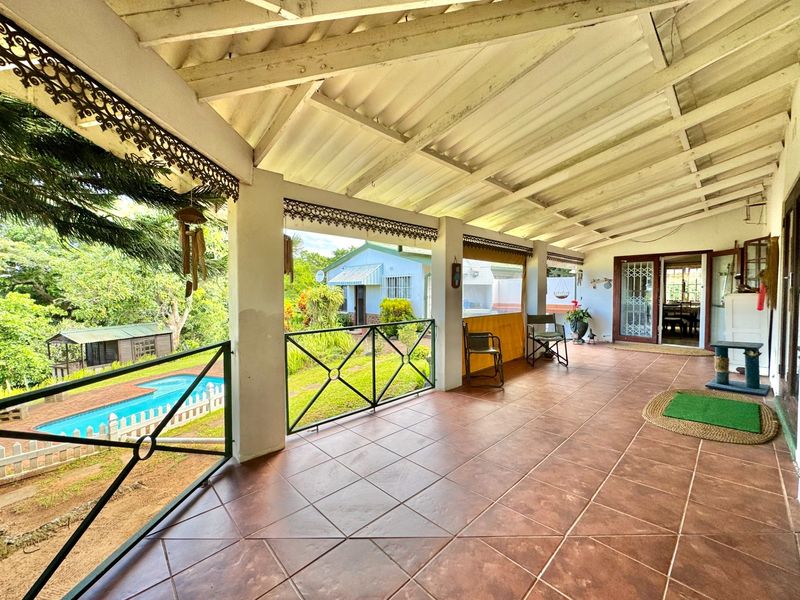 Spacious covered patio featuring tiled flooring, metal balustrades, and exposed beam ceilings, offering direct access to the garden and pool area.