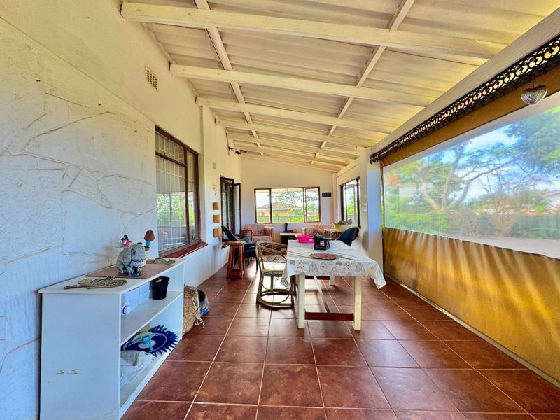 A covered patio area featuring tiled flooring, exposed beam ceiling, and a stone-clad feature wall, offering a functional outdoor living space.