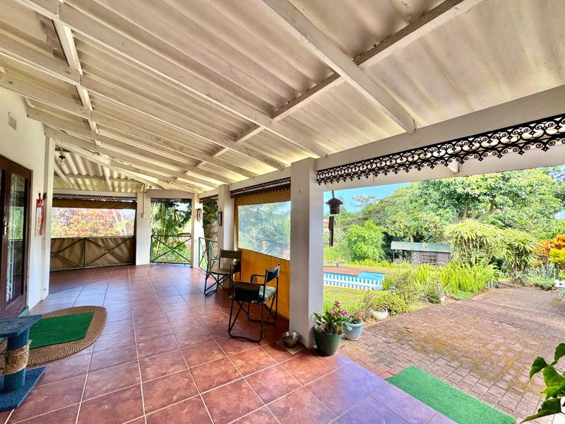 A spacious covered patio featuring tiled flooring, decorative metal detailing, and views overlooking the garden and pool area.