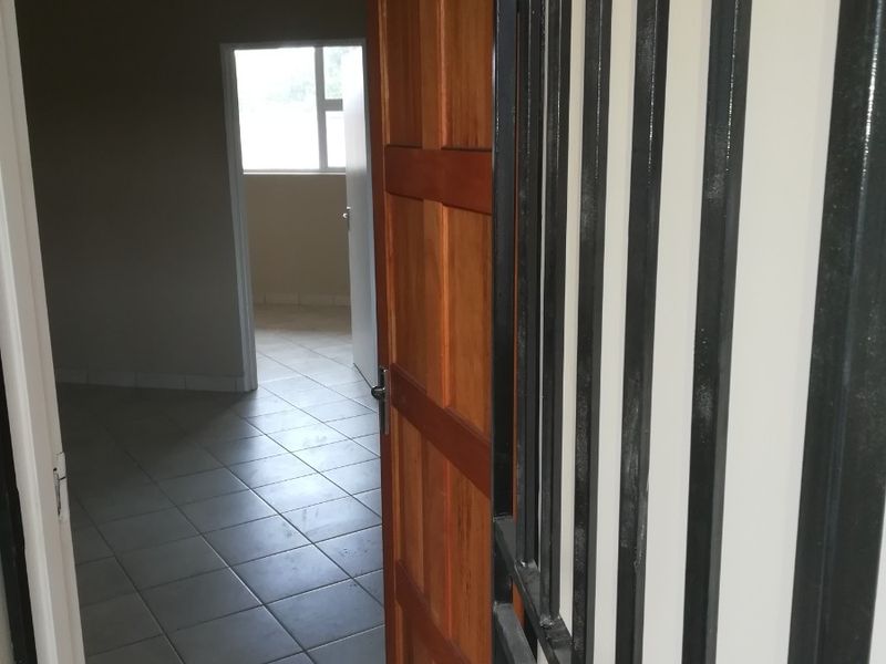 An entry area featuring a security gate and wooden door, leading into an open, tiled interior space.
