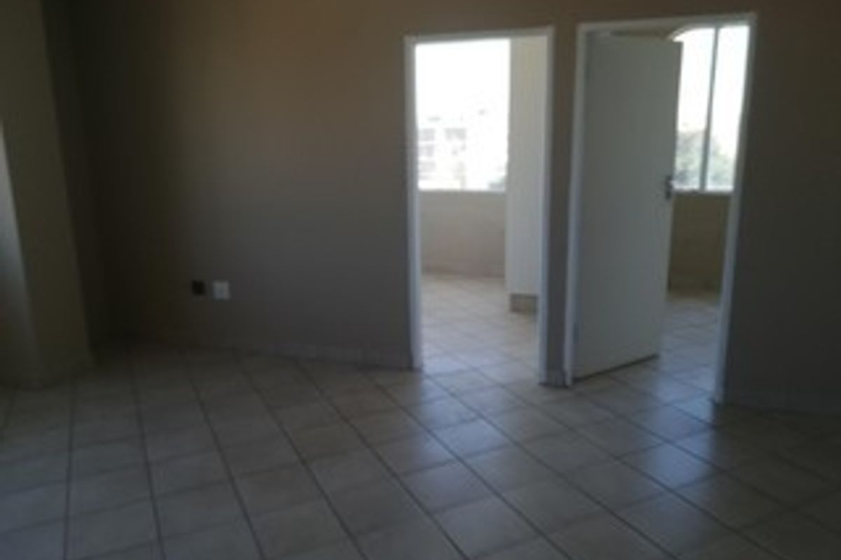 An empty living area featuring neutral tiled flooring and access to an adjoining room, providing a blank canvas for interior design.