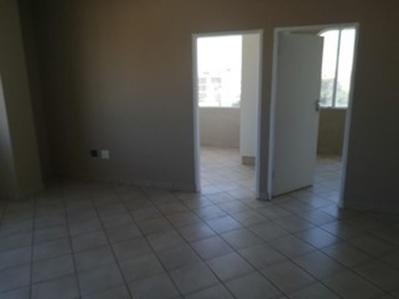 An empty living area featuring neutral tiled flooring and access to an adjoining room, providing a blank canvas for interior design.