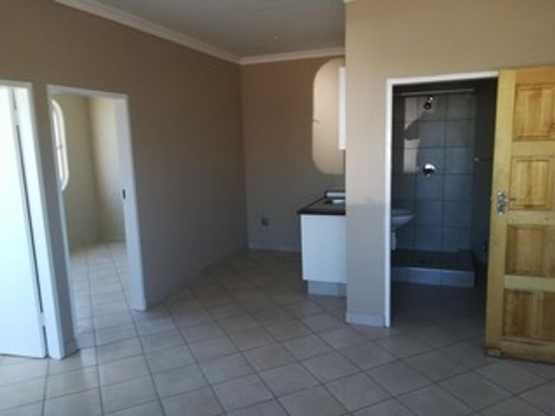 An open-plan living area featuring tiled flooring, a compact kitchen space, and direct access to an adjoining bathroom with a shower.