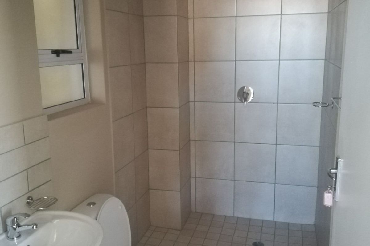A clean and functional bathroom featuring a walk-in shower, pedestal washbasin, and toilet with neutral ceramic tiling throughout.