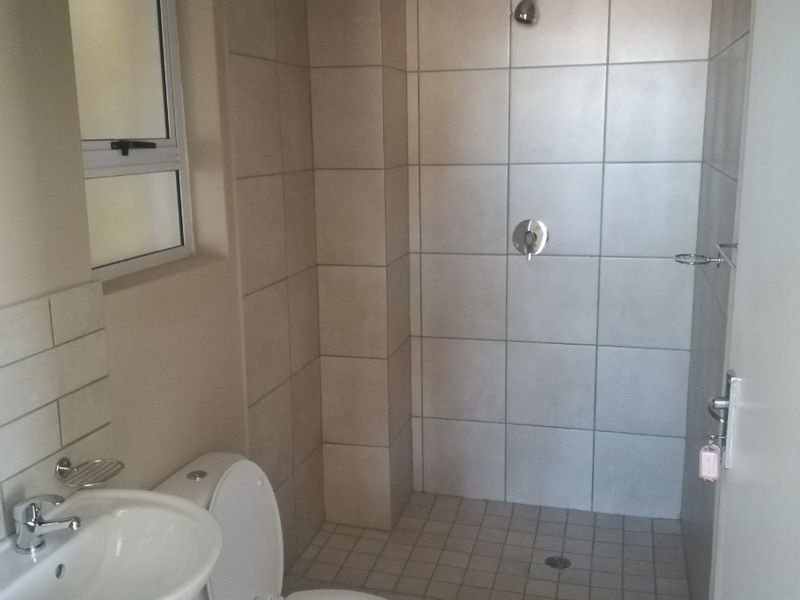 A clean and functional bathroom featuring a walk-in shower, pedestal washbasin, and toilet with neutral ceramic tiling throughout.