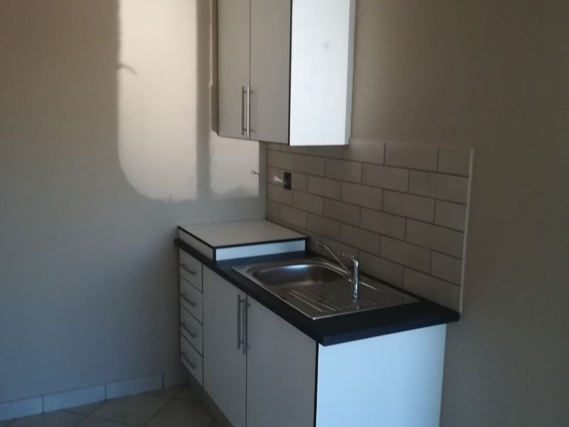 A compact kitchen area featuring white built-in cabinetry, a stainless steel sink, subway tile backsplash, and tiled flooring, currently in an unfinished state.