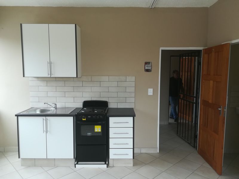 A compact kitchen featuring white cabinetry, a subway tile backsplash, a stainless steel sink, and a freestanding stove, with tiled flooring throughout.