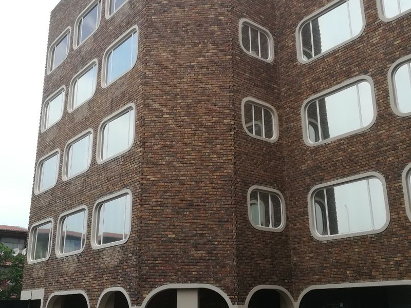 A multi-story apartment building featuring a distinctive brick facade, rounded window frames, and an arched ground-level colonnade.