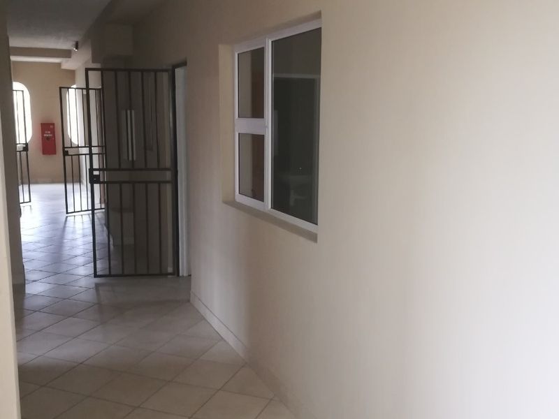 A clean, tiled apartment hallway featuring a security gate and a window, providing access to the building's common areas.