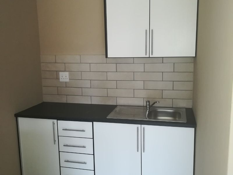 A compact kitchen area featuring white built-in cabinetry, a stainless steel sink, subway tile backsplash, and neutral tiled flooring.