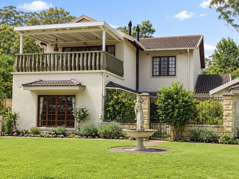 Rear view of a two-story residence featuring a covered balcony, tiled roof, timber-framed windows, and a well-maintained garden with a central fountain.
