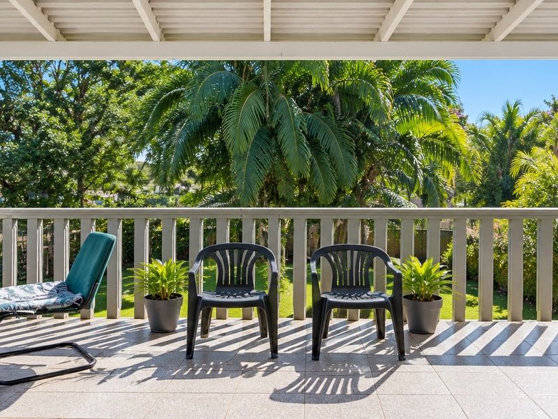 A covered balcony featuring tiled flooring and a protective railing, offering a pleasant outdoor space with views of the surrounding greenery.