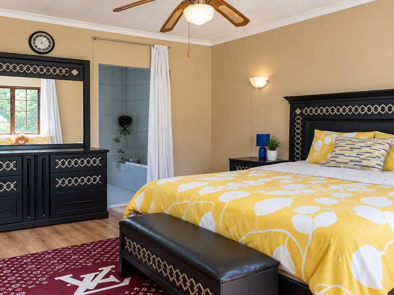 Spacious bedroom featuring a ceiling fan, wall lighting, and direct access to an en-suite bathroom with a bathtub.