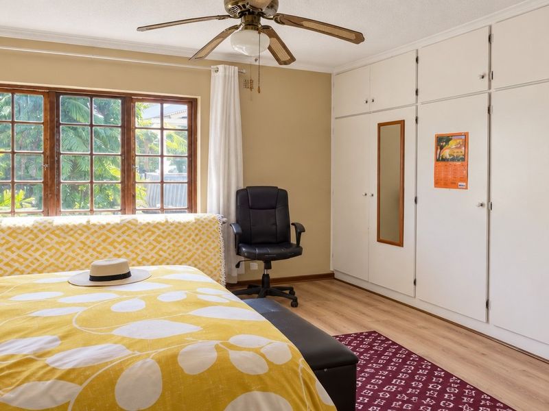 A well-lit bedroom featuring extensive built-in cupboards, a ceiling fan, and laminate flooring, offering a functional and comfortable living space.