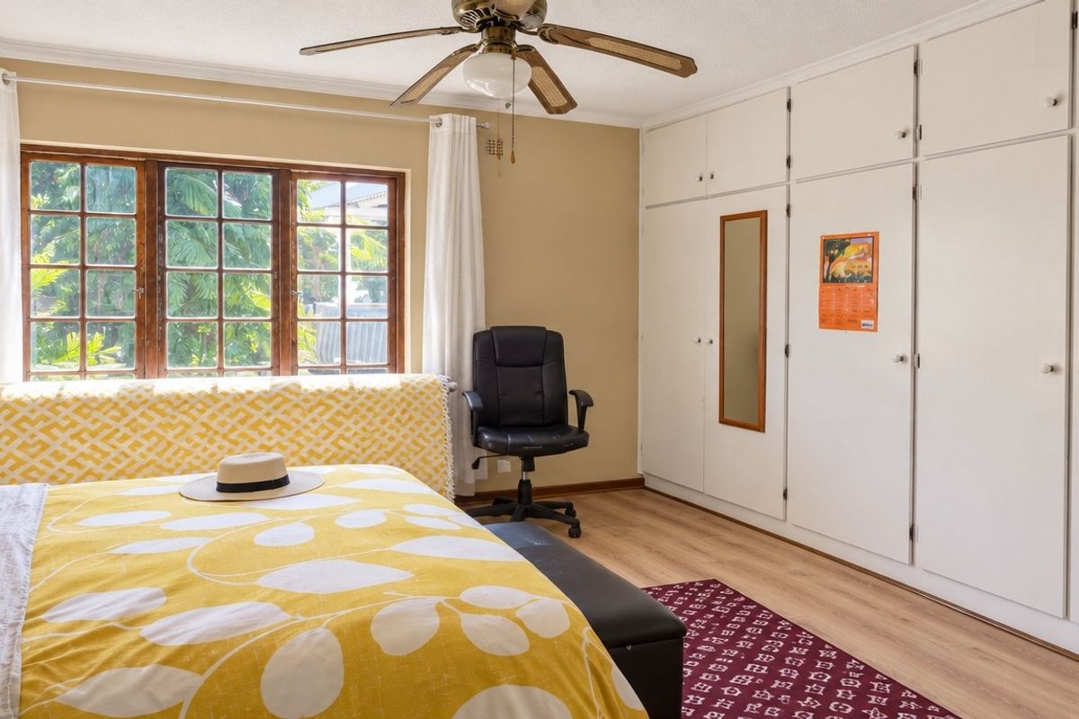 A well-lit bedroom featuring extensive built-in cupboards, a ceiling fan, and laminate flooring, offering a functional and comfortable living space.
