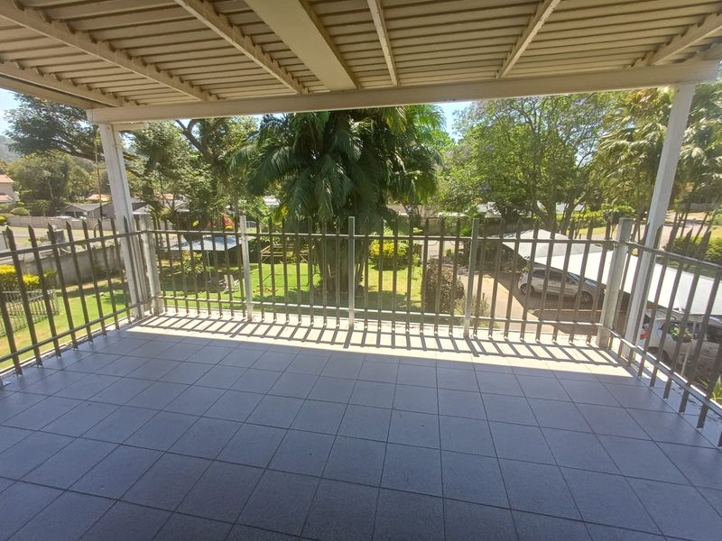 A covered balcony featuring tiled flooring and a metal balustrade, offering an elevated view of the surrounding garden and neighborhood.