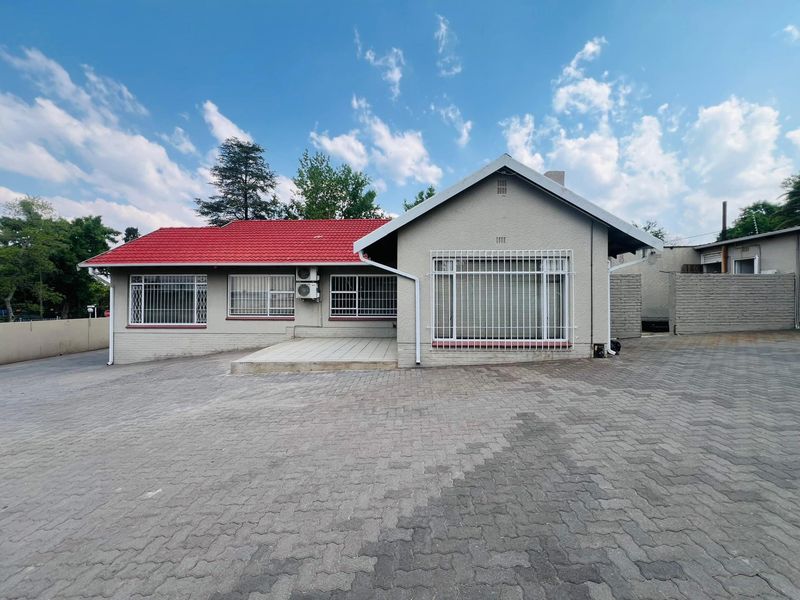 Front exterior view of a commercial property featuring a paved driveway, tiled roof, and security bars on windows.