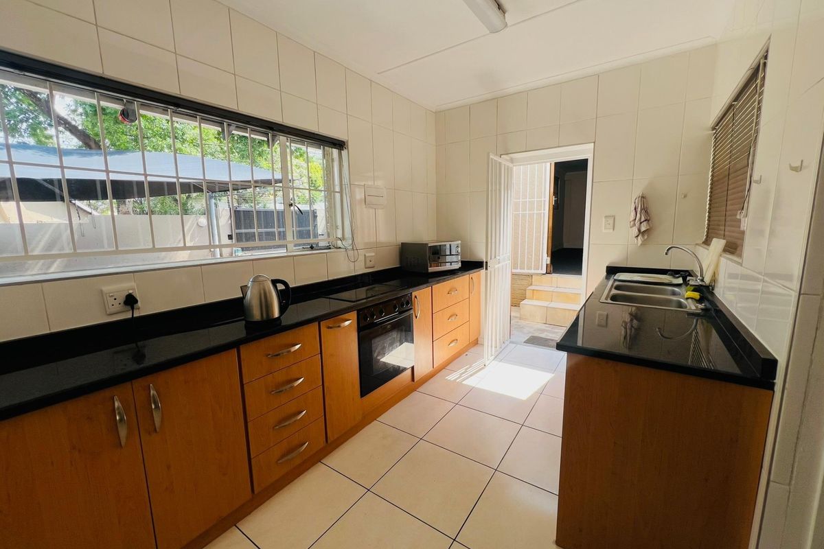 Functional kitchen featuring wooden cabinetry, granite countertops, built-in oven, hob, and double sink with tiled finishes and direct access to the exterior.