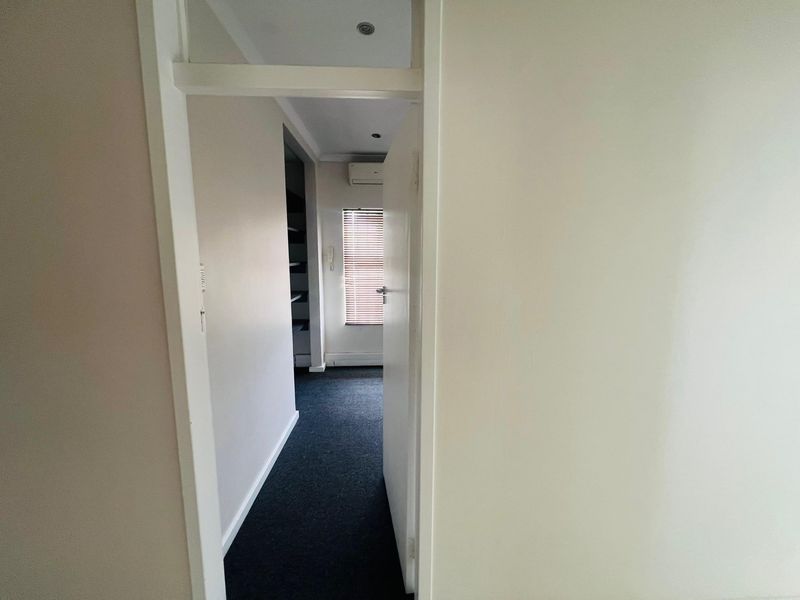 A view through a doorway into a carpeted hallway featuring recessed lighting, an air conditioning unit, and window blinds.