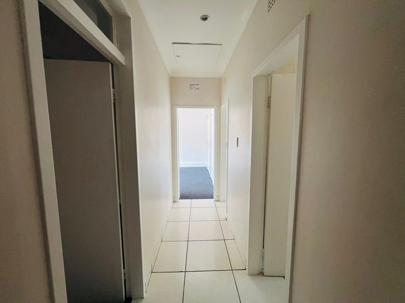 A clean, empty hallway featuring white walls, tiled flooring, and recessed ceiling lighting, providing access to multiple rooms.