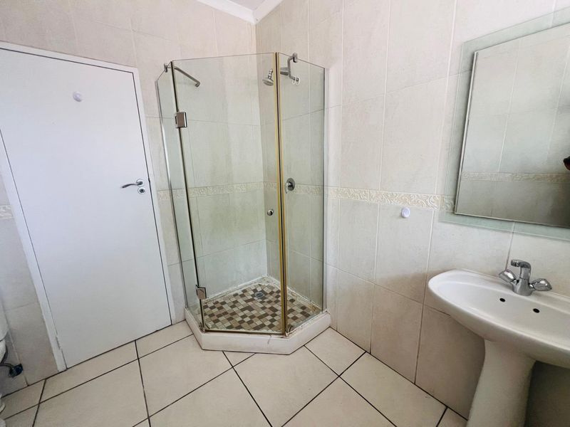 A functional bathroom featuring a corner shower enclosure, pedestal basin, and neutral ceramic wall and floor tiling.