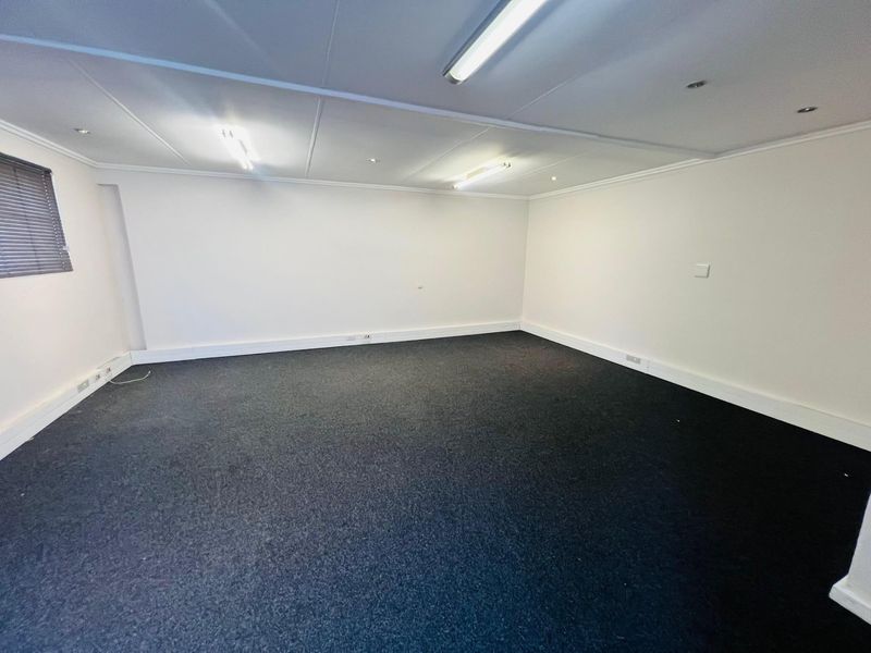 A clean, empty commercial office space featuring neutral walls, dark carpeting, and functional overhead lighting, suitable for a variety of business configurations.