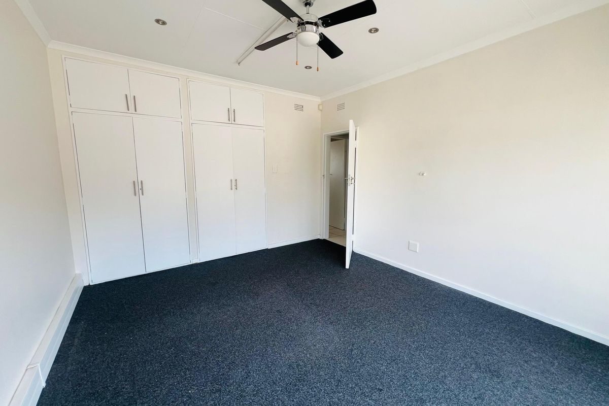 A clean, empty bedroom featuring built-in cupboards, a ceiling fan, and dark carpeting, offering a neutral space ready for customization.