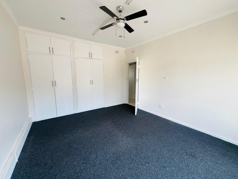 A clean, empty bedroom featuring built-in cupboards, a ceiling fan, and dark carpeting, offering a neutral space ready for customization.