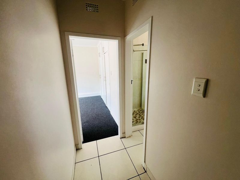 A functional hallway featuring tiled flooring, providing access to a bedroom with built-in cupboards and a separate shower room.