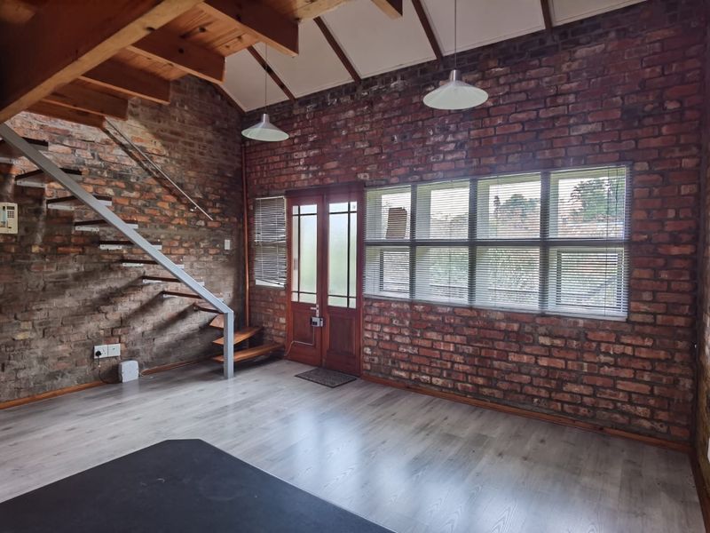 Spacious living area featuring exposed brick walls, timber staircase, and laminate flooring, offering a rustic industrial aesthetic with abundant natural light.