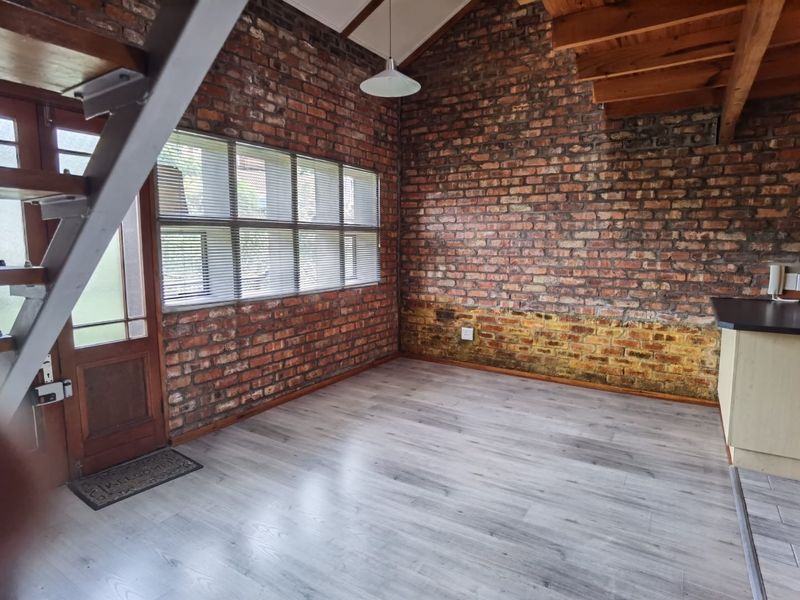 Open plan living area featuring exposed brick walls, laminate flooring, and a timber staircase leading to a mezzanine level.