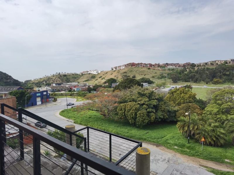 Elevated view overlooking the surrounding neighbourhood, green spaces, and distant hillside residential developments from a balcony with a metal balustrade.